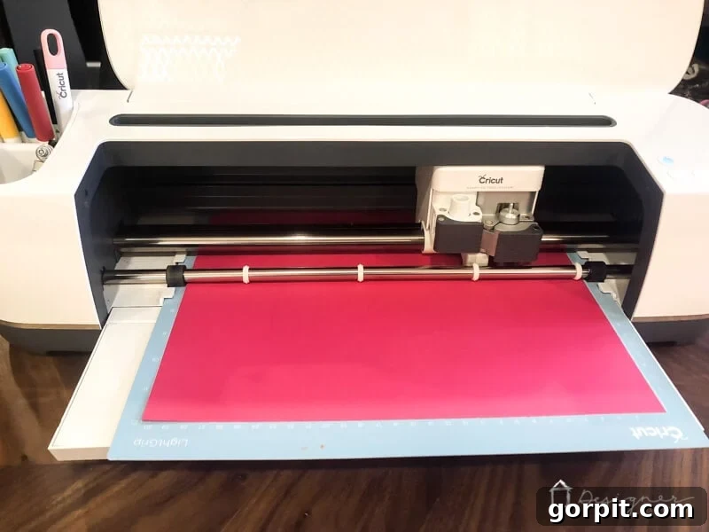 Elevate Your Photos: DIY Mats on a Budget 4 A Cricut cutting machine precisely cutting a custom design into pink cardstock for a picture mat.