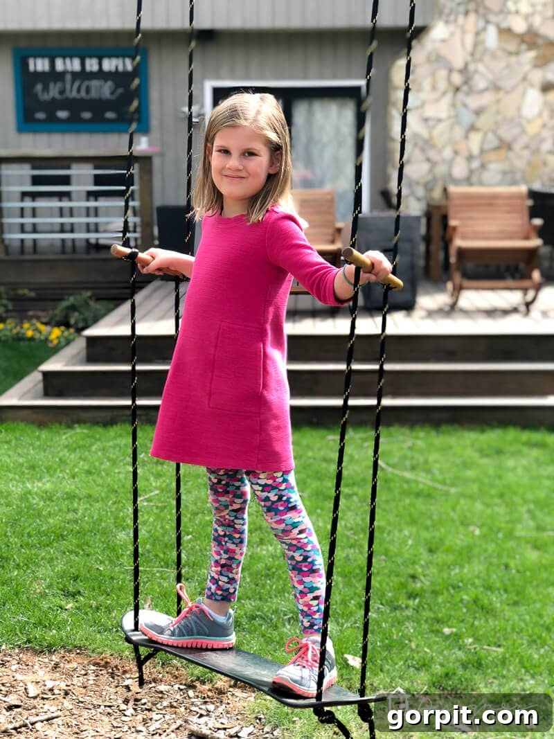 A child joyfully standing and swinging on the newly installed DIY skateboard swing in a green backyard.