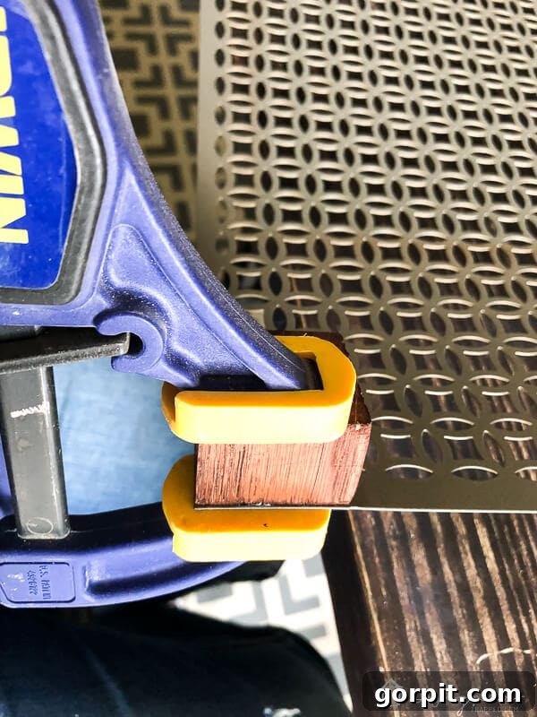 Tangle-Free Treasures: Easy DIY Jewelry Organization 8 A stained wood block firmly clamped to the corner of a decorative aluminum sheet.