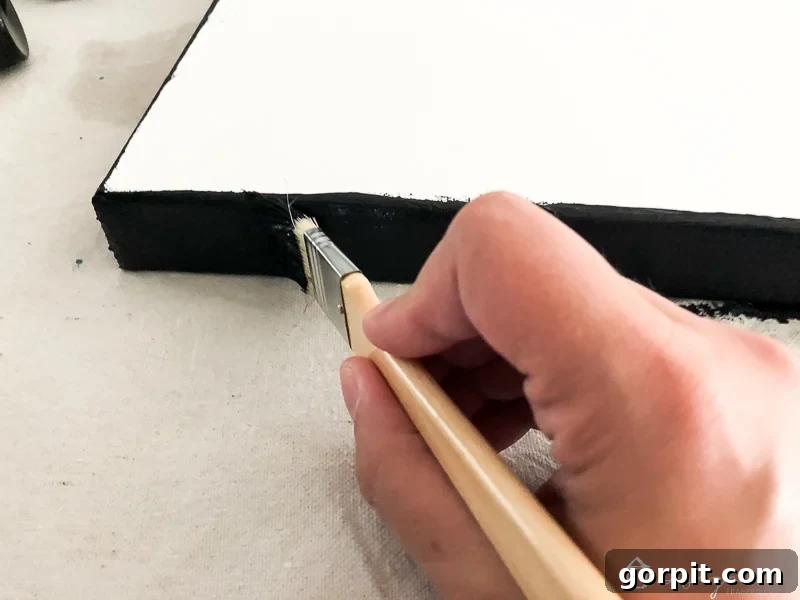 Painting the dark navy blue edges of a DIY abstract canvas