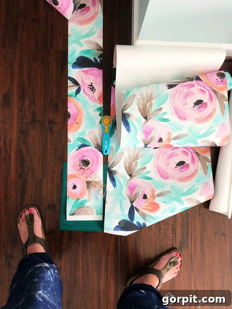 Hands carefully applying a final strip of temporary floral wallpaper, overlapping to match the pattern perfectly.