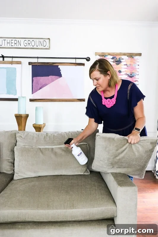 Sofa Freshness Hacks 5 Tasha applies Mohawk Fabric Guard to her sectional couch located in a bright room with a rod of colorful artwork behind it.