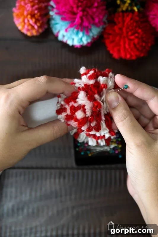 Hands pinning colorful pom poms onto a foam wreath form