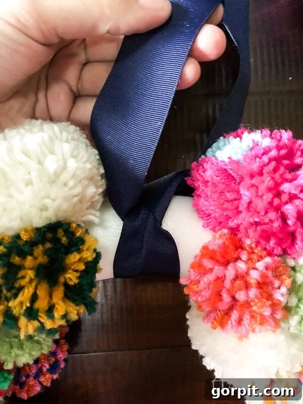 Tying a navy blue ribbon onto a colorful DIY pom pom wreath