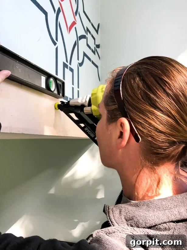 Attaching first wood plank to wall with nail gun and level