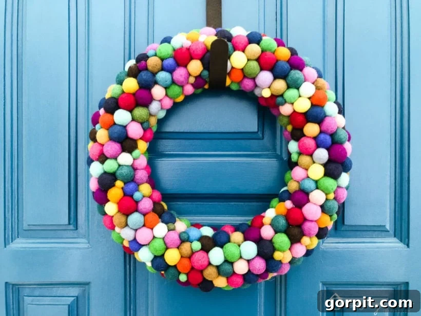 The finished colorful DIY felt ball wreath hanging elegantly on a deep blue door, showcasing its vibrant appeal