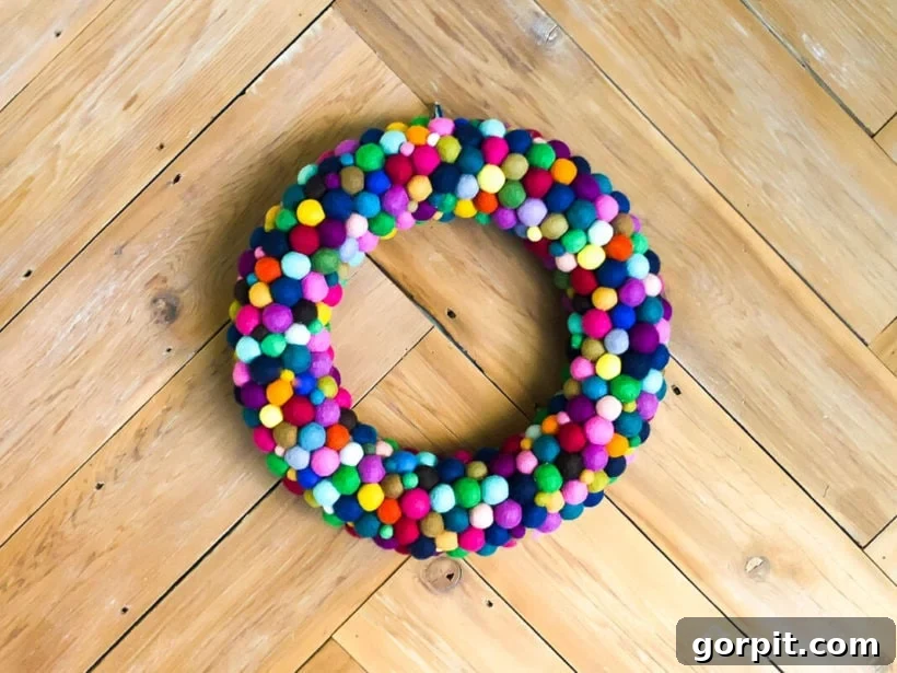 Another view of the finished colorful DIY felt ball wreath, displayed against a rustic wood wall, highlighting its texture and charm