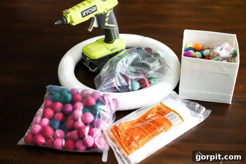 All the essential supplies for making a felt ball wreath, including colorful felt balls, foam wreath form, hot glue gun, and ribbon