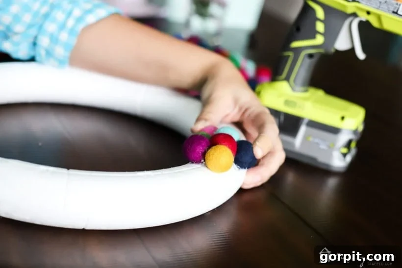 Another perspective of the crafting process, showing colorful felt balls being meticulously glued onto the wreath base
