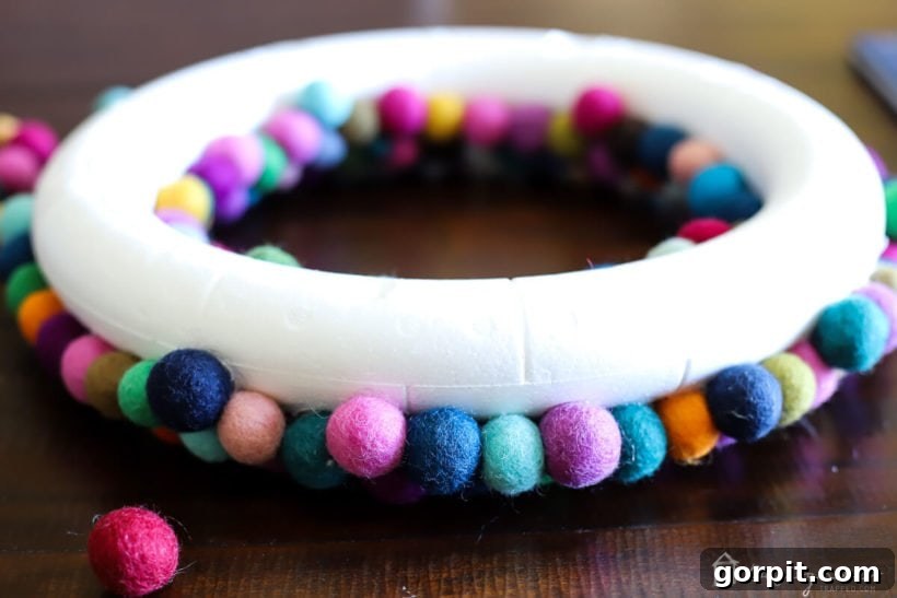 An in-progress shot of the colorful DIY felt ball wreath, showing more felt balls being added to the sides for full coverage