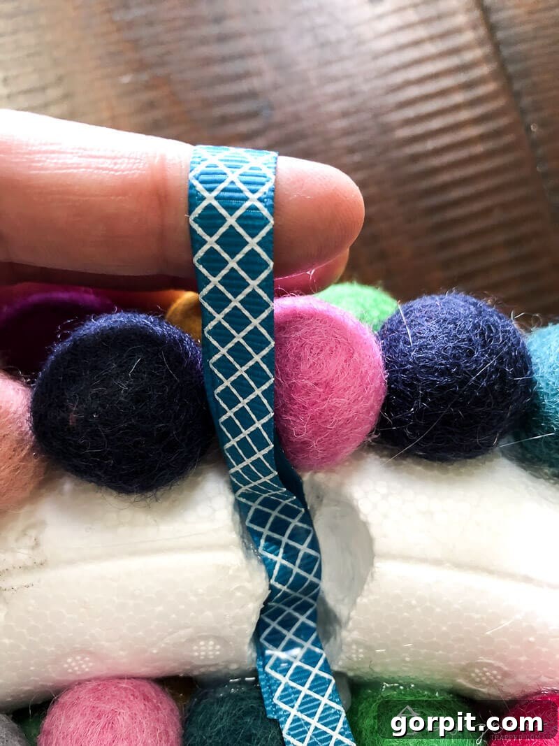 Demonstration of attaching a ribbon to the back of the felt ball wreath using hot glue, preparing it for easy hanging