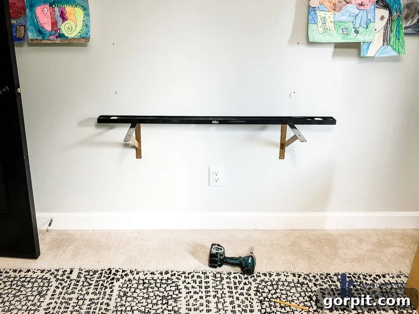 hanging wall brackets for DIY floating desk by Tasha Agruso of Kaleidoscope Living, showing a bracket being leveled and secured to a wall