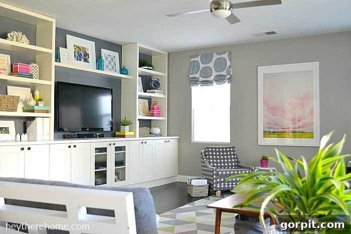 Transform Your IKEA: Bookshelf & Cabinet Built-In Hacks 10 A tastefully designed living room features built-ins crafted from IKEA kitchen cabinets and shelves, spanning the entire wall. This custom unit elegantly houses a television, a curated collection of books, and various decorative knick-knacks, creating a harmonious and functional entertainment space.