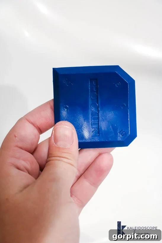 Fingers hold up a blue caulk-smoothing tool, ready for use.