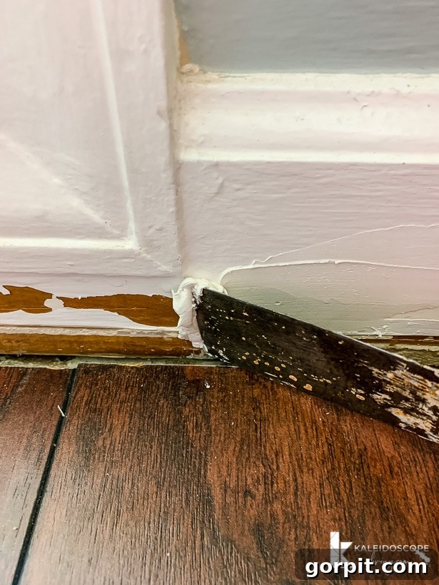Easy Ways to Repair Chipped Baseboards 5 Applying spackle to a damaged baseboard with a putty knife at a 45-degree angle, demonstrating the technique