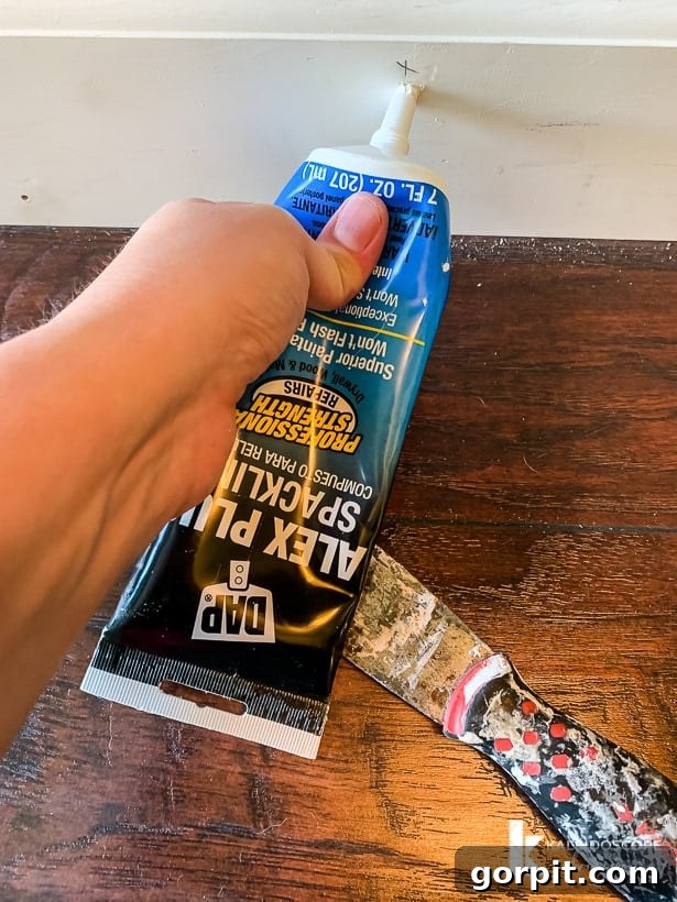 Easy Ways to Repair Chipped Baseboards 7 Using DAP Alex Plus Spackling to fill small nail holes in baseboard, demonstrating a quick fix