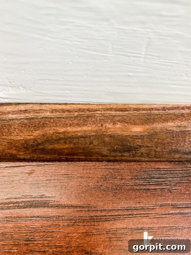 Your Guide to Perfect Quarter-Round Molding 12 A close-up of stained quarter round molding against a wood floor showing that nail holes are covered by near invisible putty, demonstrating a professional finish.