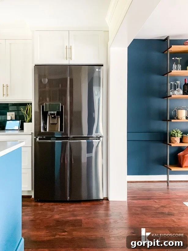 Your Guide to Perfect Quarter-Round Molding 13 A white kitchen and a navy-blue dining room with a shiny refrigerator in the center, showcasing the newly installed quarter round molding. KaleidoscopeLiving.com and the K logo are in the corner.