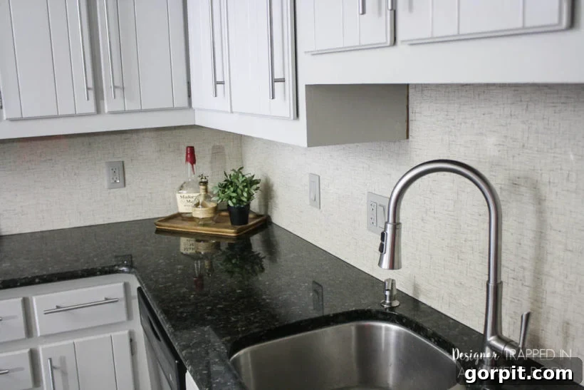 A white kitchen with dark countertops features a simple white Formica backsplash. 