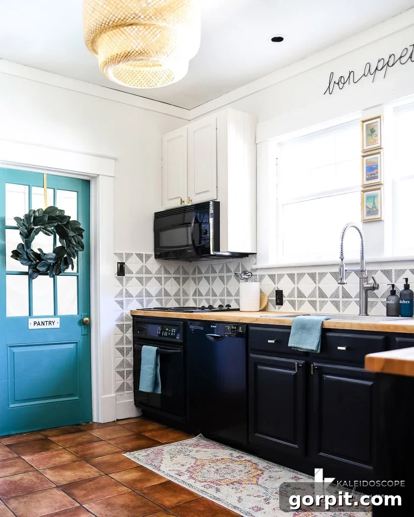 Small Budget Big Impact DIY Kitchen Transformation 14 A kitchen corner with a blue door with a wreath and a sign that says "pantry," partial tiled walls, white upper cabinets and blackish lower cabinets.