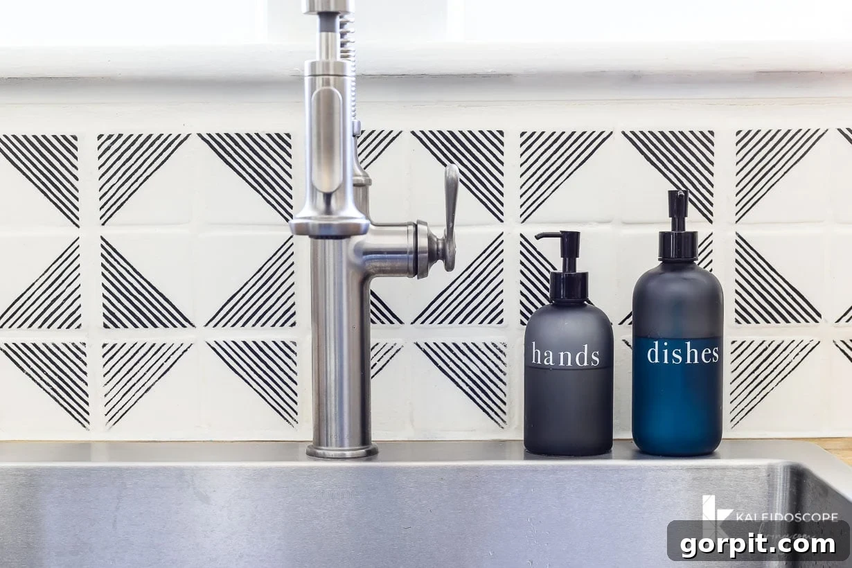 Small Budget Big Impact DIY Kitchen Transformation 19 A close-up of a faucet and a white and black geographic tile stenciled backsplash. Two pump bottles to the right of the sink say "hands" and "dishes." "KaleidoscopeLiving.com" is written in the lower right corner.