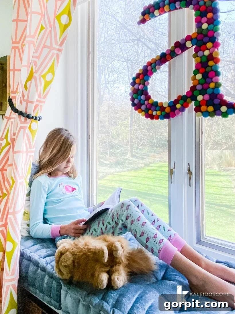 Close-up of a girl's window seat in a colorful room, showcasing decorative pillows and a DIY felt letter.