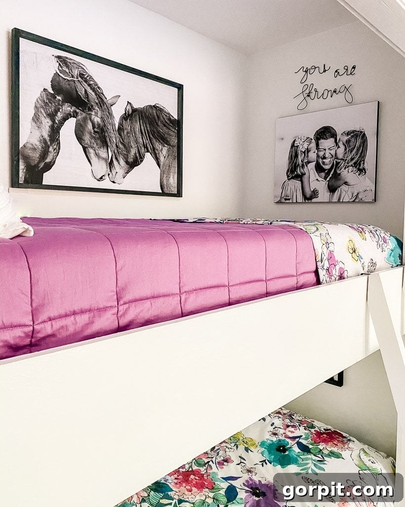 The top of this bedroom's built-in bunk beds has a pink duvet and the wall has a picture of horses, a canvas print of a father with two daughters, and a sign that says, 