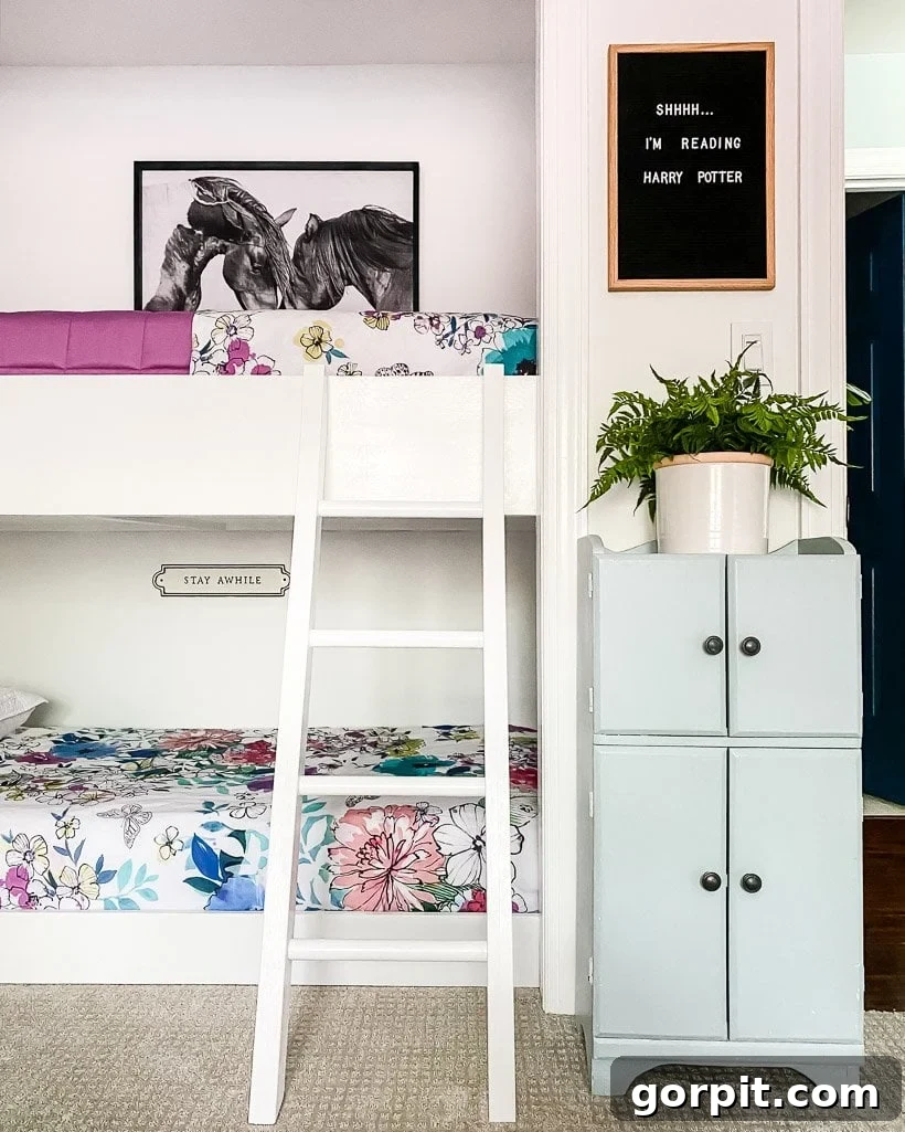Built-in bunk beds in a girl's bedroom have a white ladder, a tall set of cabinets and a sign that reads, 