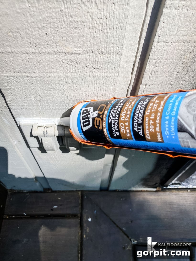 Applying caulk around an outdoor electrical outlet on house siding