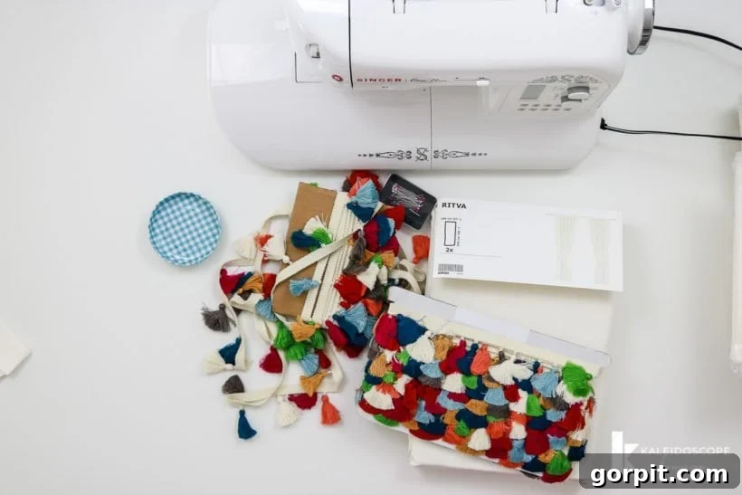 Crafting station with a sewing machine, colorful tassel trim, and white curtain fabric laid out, ready for the DIY curtain project.