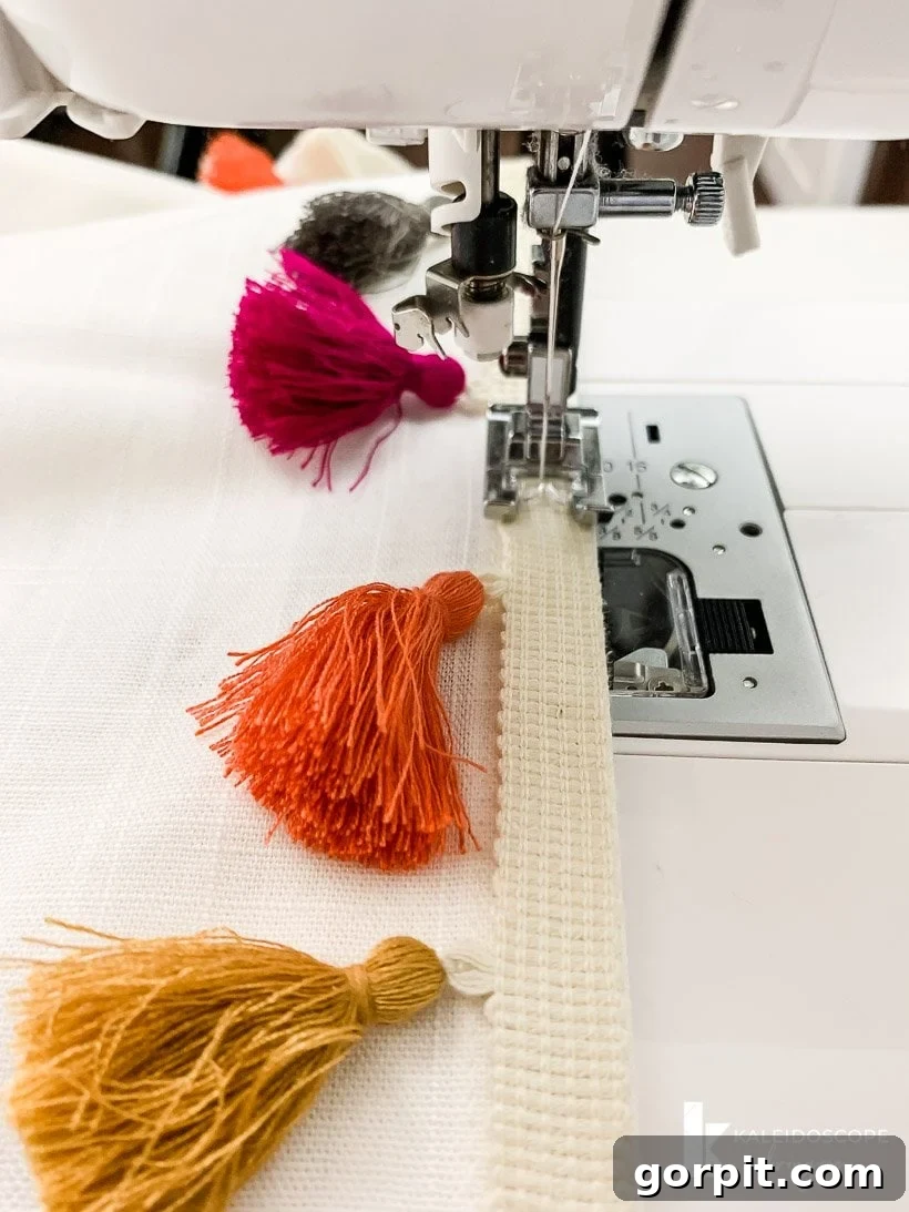 A sewing machine expertly stitching colorful tassel trim onto a white curtain panel, demonstrating the attachment process.