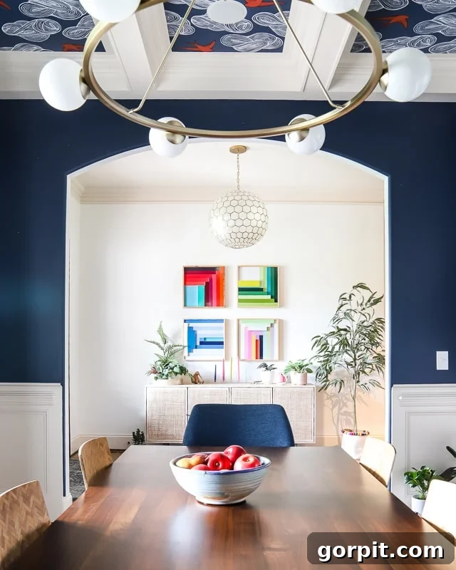Welcome to Our Navy Dining Room 7 A dining room painted Gale Force blue, with a wallpaper and painted coffered ceiling looking into the white foyer with four colorful pieces of square art on the wall.