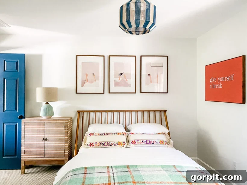 Designer-Approved Bedroom Wall Art Ideas 5 A bright and colorful guest room featuring a unique gallery wall with a trio of abstract prints and a custom 'give yourself a break' sign.
