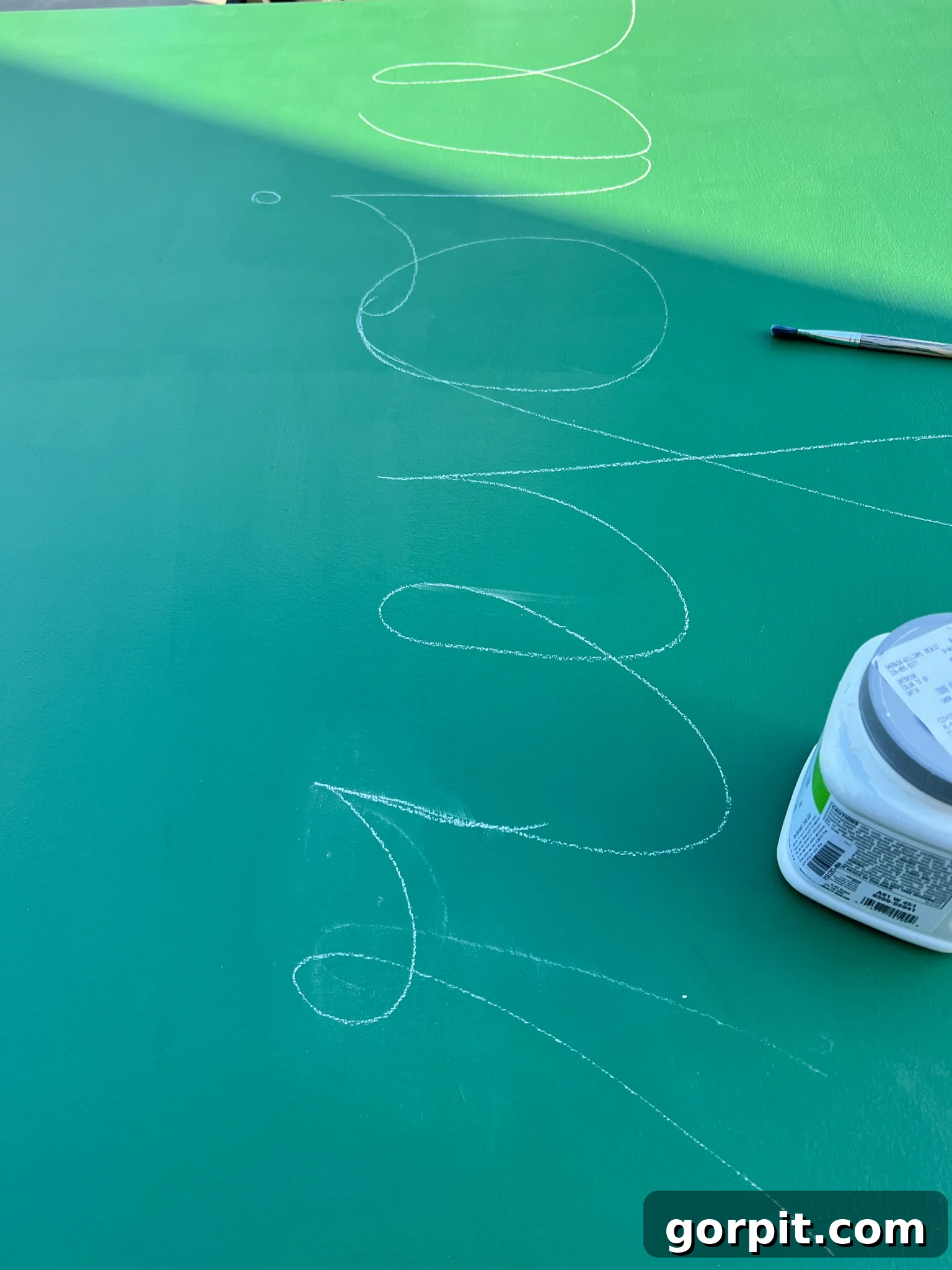 Chalk outline of 'Rejoice' sketched onto green painted plywood.