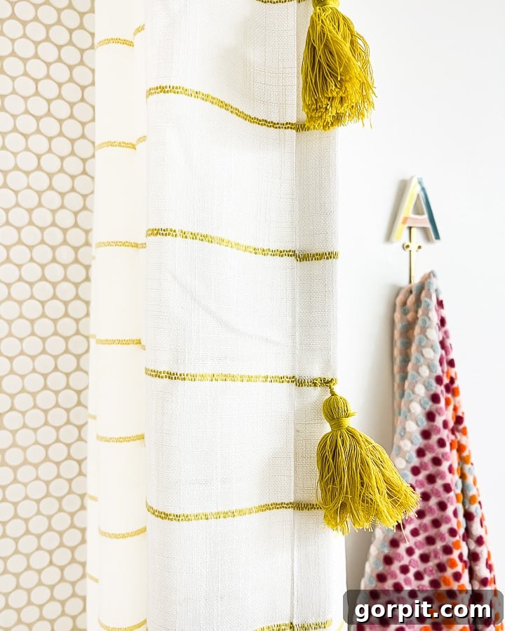Round tiles in the shower with white and gold curtains with gold tassels next to a fun towel hook with the letter "A" on top. 