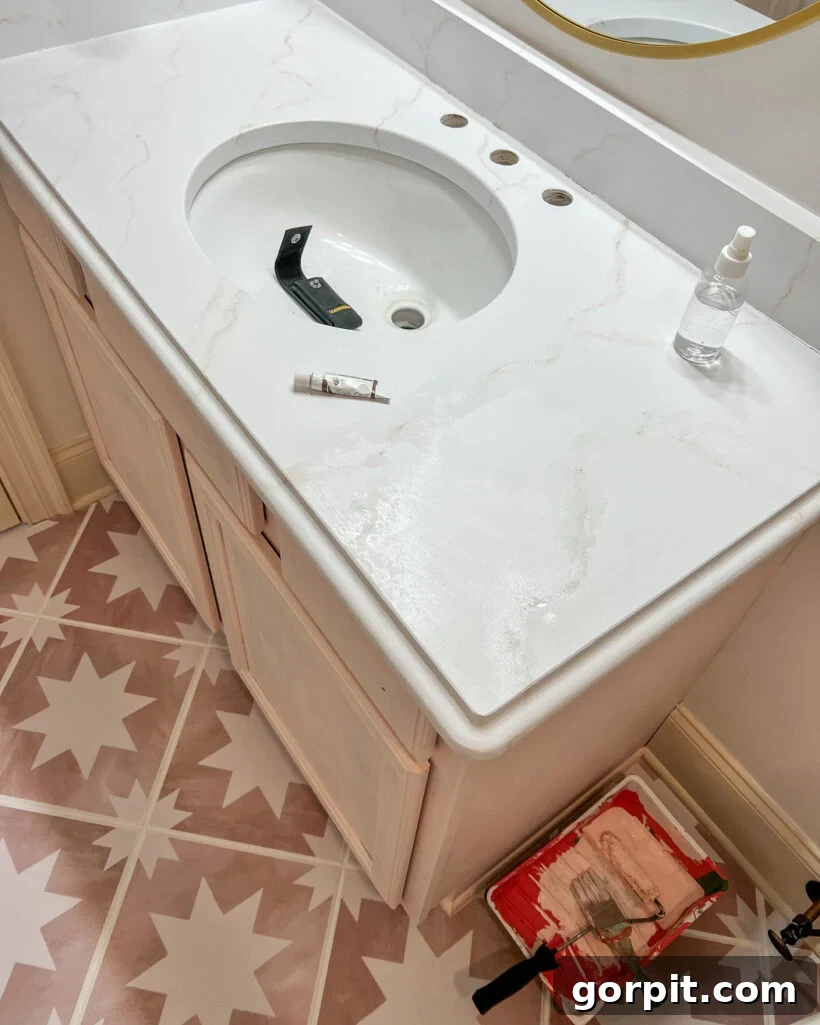 An overhead view of a bathroom countertop painted to look like white marble, with a light pink under-cabinet and geometric flooring. 