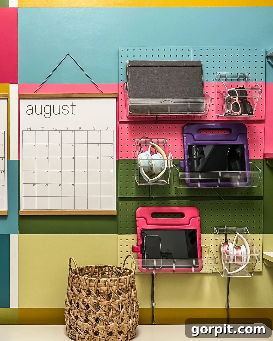 A vibrant wall-mounted family charging station utilizing a colorful pegboard to hang acrylic trays and a practical calendar that reads, "August." This DIY solution effectively organizes electronic devices.