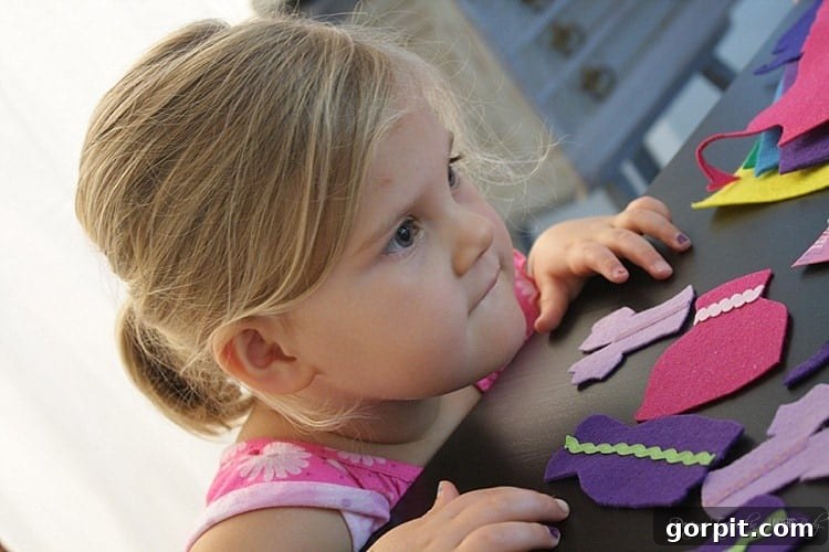 Two young girls intently focusing on their felt doll craft project, with various colorful felt pieces and completed doll clothes spread around them.