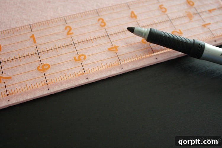 A ruler placed on a piece of sticky stiff felt, with a marker making incremental marks along the edge for punching holes for the doll book binding.