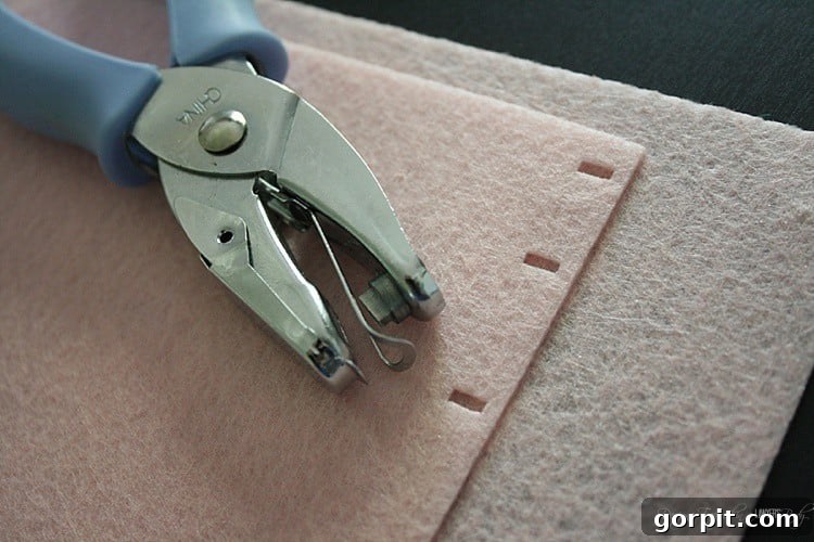 A hand operating a rectangle hole punch on a marked piece of stiff felt, creating perfectly aligned holes for the book's spine.