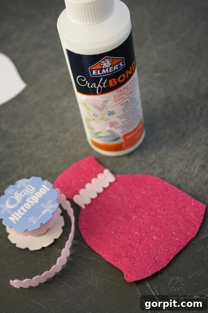 Little hands of a child carefully gluing a small pom-pom onto a felt doll dress, illustrating the hands-on and creative aspect of the DIY project.