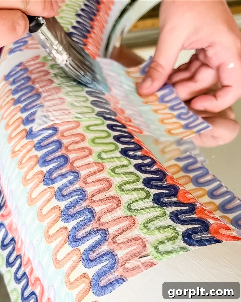 Applying decoupage medium over a napkin on a mirror frame