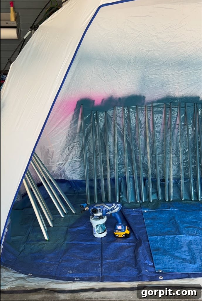 Painting new wooden balusters with a paint sprayer inside a portable spray shelter