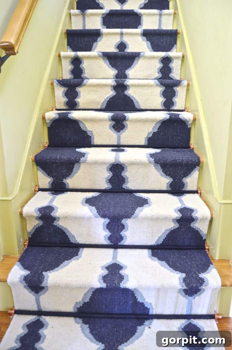 Merdivenlerinizi Şıklaştırın: İlham Veren Koşucu Halı Fikirleri 16 A budge- friendly blue and white graphic stair rug sits against yellow walls and black stair rods.