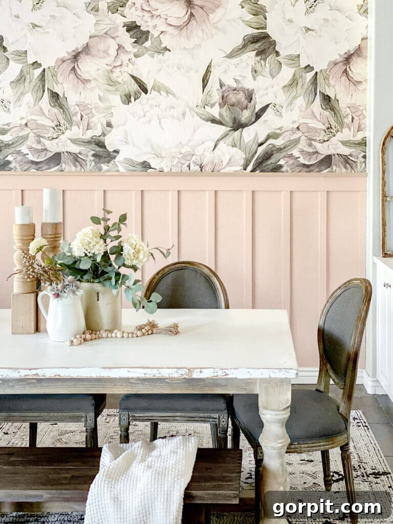 Transform Your Walls with DIY Board and Batten 12 A stylish dining table is beautifully set against a soft pink board and batten wall, which is elegantly complemented by expansive floral wallpaper, creating a charming and inviting atmosphere.