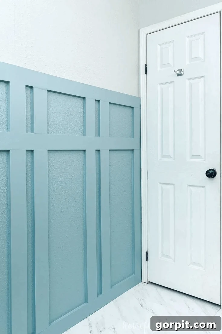 Transform Your Walls with DIY Board and Batten 4 A contemporary blue board and batten bathroom wall stands out against crisp white accents, a door, and light flooring. The accent wall features distinctively spaced battens, giving it a modern and airy feel.