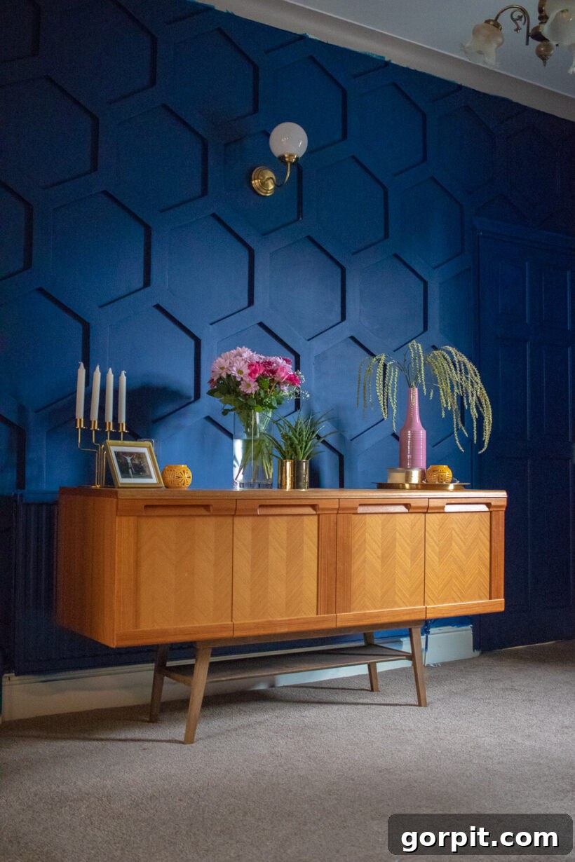 Transform Your Walls with DIY Board and Batten 10 An intriguing deep blue wall is designed with a hexagon-shaped board and batten pattern, creating a modern and artistic backdrop behind a stylish mid-century modern sideboard adorned with decorative pieces.