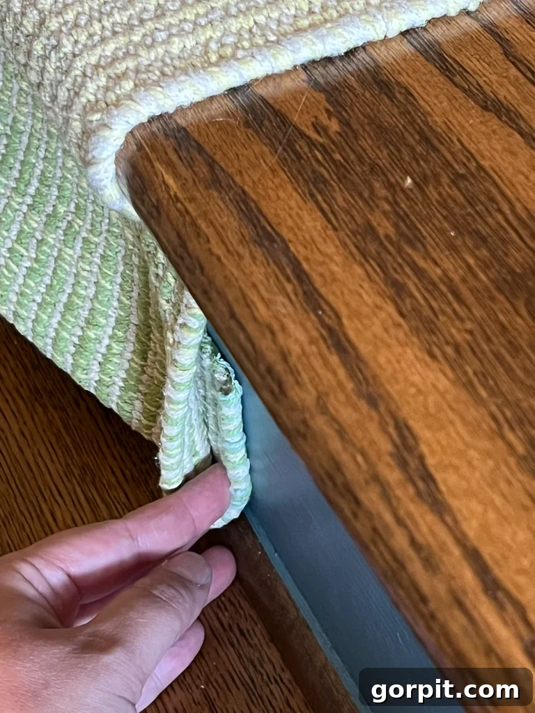 Securing the bottom end of a DIY stair runner by folding and stapling excess material against the riser
