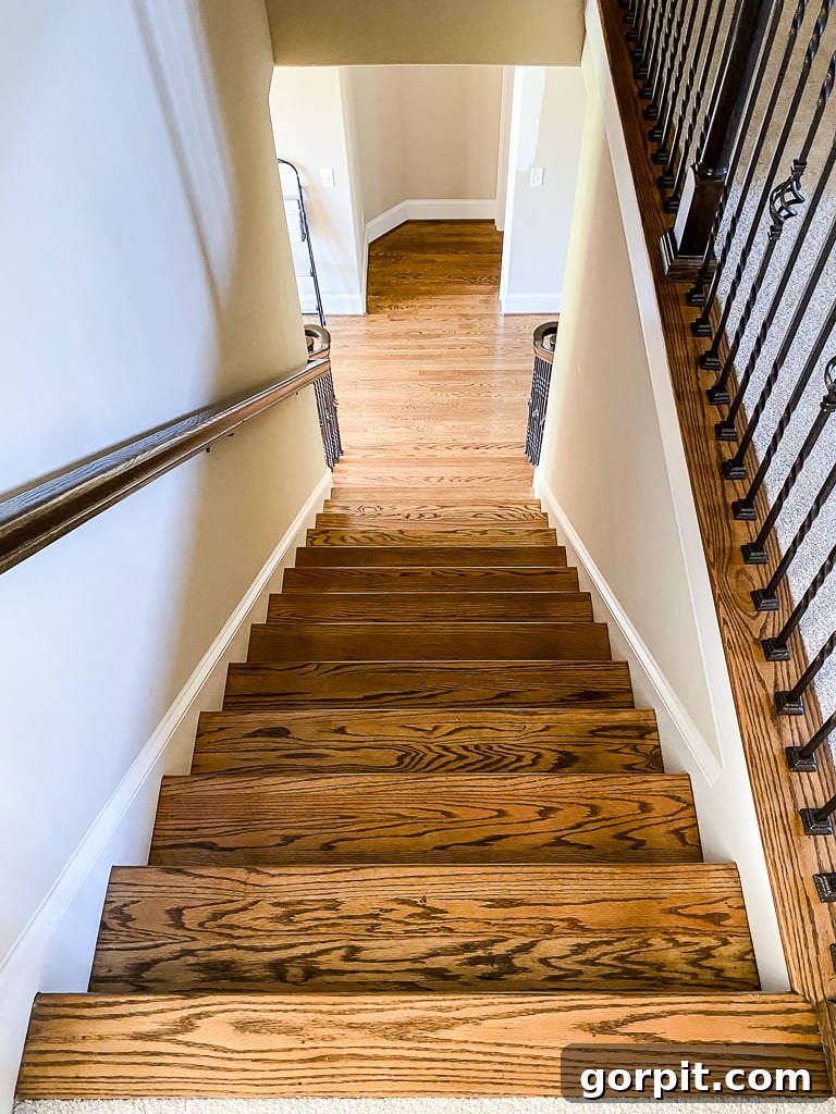 Dated beige staircase with simple iron balusters and plain wood floors, illustrating the 'before' transformation
