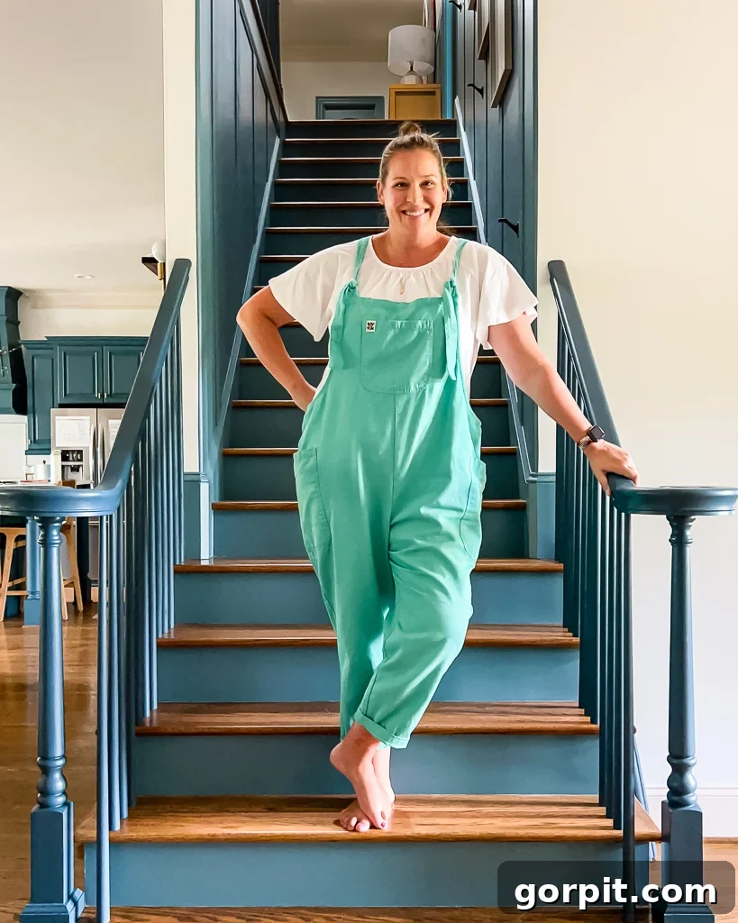 Tasha Agruso standing on a staircase during the renovation, showing freshly painted stairs and new balusters, before the runner